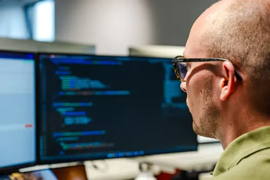 IT-expert van Harbers Group werkt achter computer met programmeercode op het scherm – illustratie van softwareontwikkeling, technische expertise en digitale innovatie.