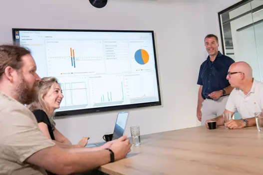 Overleg tussen IT-experts bij scherm met grafieken – representatie van strategisch advies en technische expertise.