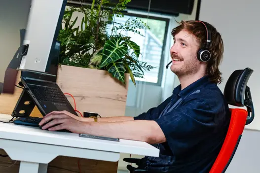 IT-supportmedewerker met headset achter computer, in gesprek met klant