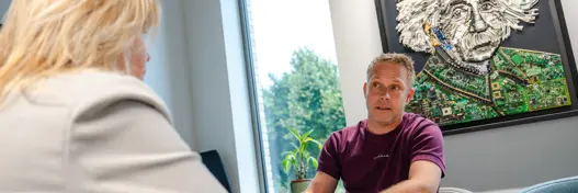 Collega en klant in overleg aan tafel, in gesprek over IT-oplossingen en samenwerking.