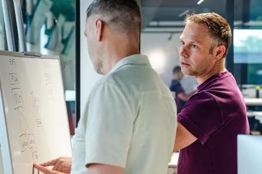 Twee engineers overleggen bij een whiteboard over datacenterstructuur en beveiligingsmaatregelen