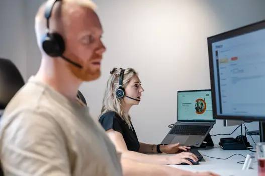 Twee supportmedewerkers met headset achter hun computer, klaar om klanten te helpen met IT-support op afstand