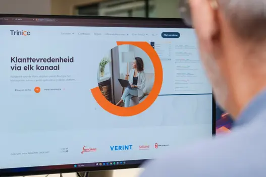 Beeldscherm met de website van TriniCo.io in beeld, met op de achtergrond een IT-expert van Harbers Group