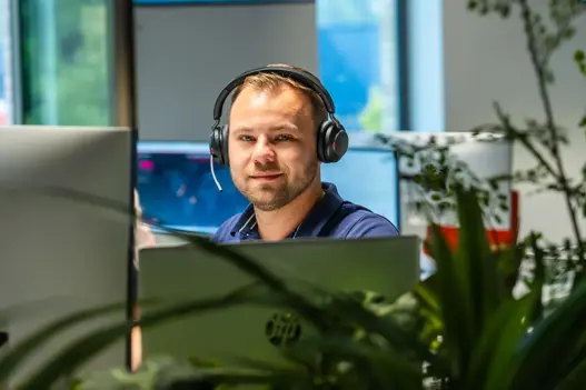IT-supportmedewerker met koptelefoon achter beeldscherm, klaar om klanten te ondersteunen