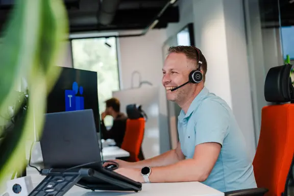 IT-engineer van Harbers Group met headset achter computer, lachend in gesprek met klant