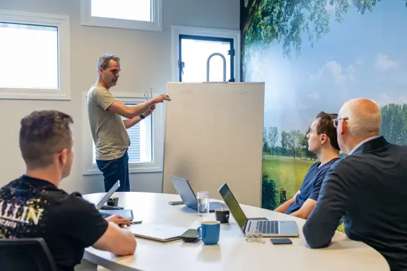 Teamoverleg bij Harbers Group in vergaderruimte met presentatie aan whiteboard – kennisdeling, samenwerking en digitale strategie in actie.