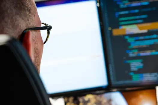 IT-specialist werkt geconcentreerd achter computer met programmeercode op het scherm, symbool voor technische expertise en softwareontwikkeling.