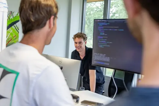 IT-expert glimlacht vriendelijk naar collega’s achter computer