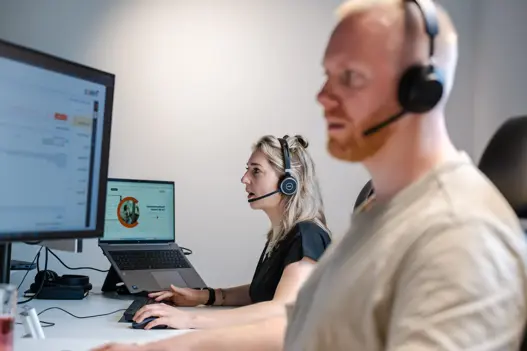 Twee supportmedewerkers met headset achter hun computer, klaar om klanten te helpen met IT-support op afstand