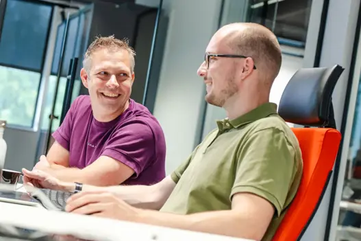 Twee IT-experts van Harbers Group zitten achter hun computer in overleg met plezier